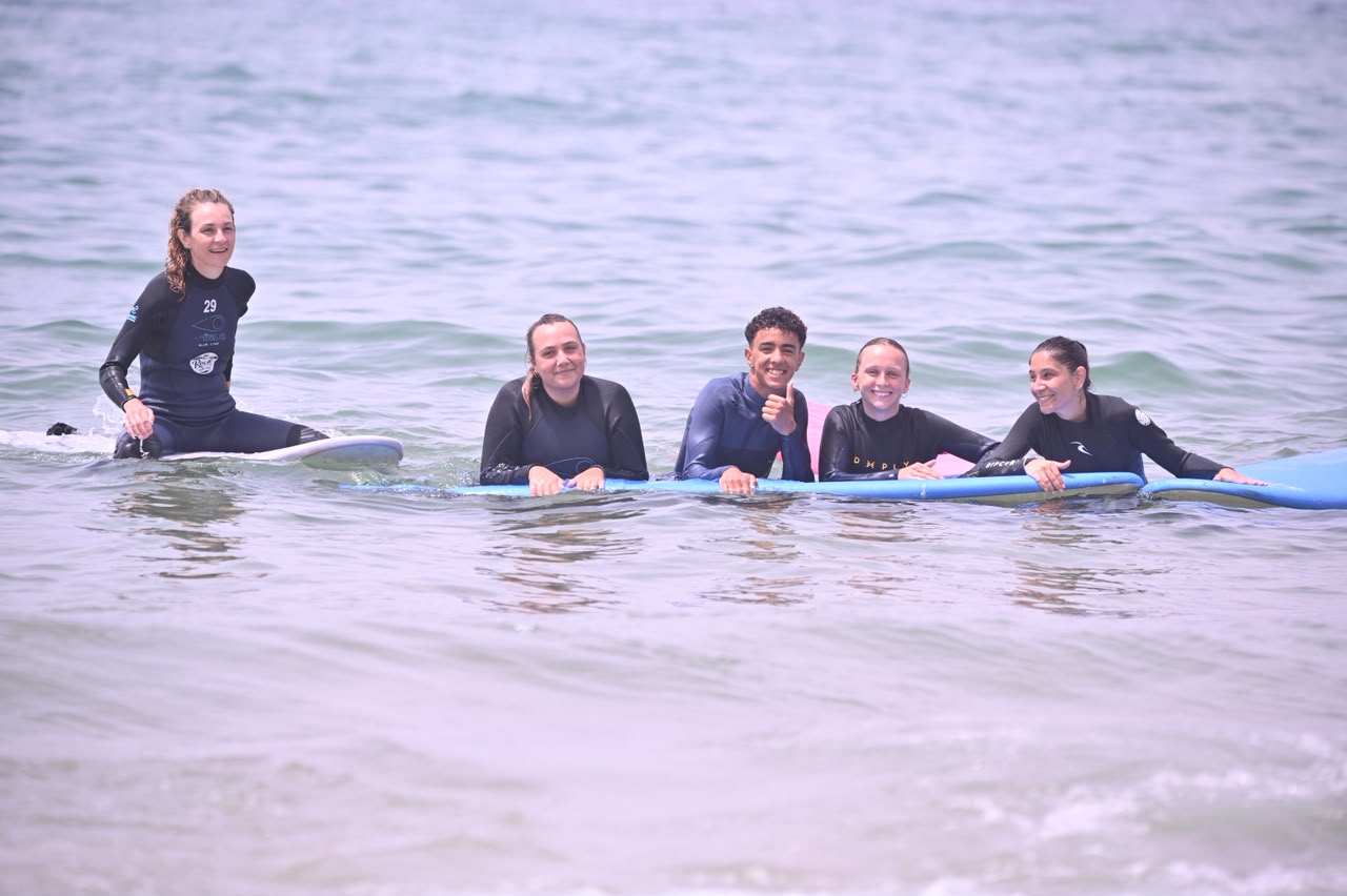 Four surfers on boards in flat water, smiling